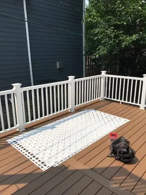 Gallery. A white mat on a wood deck with white railing, next to a dark backpack and water bottle.