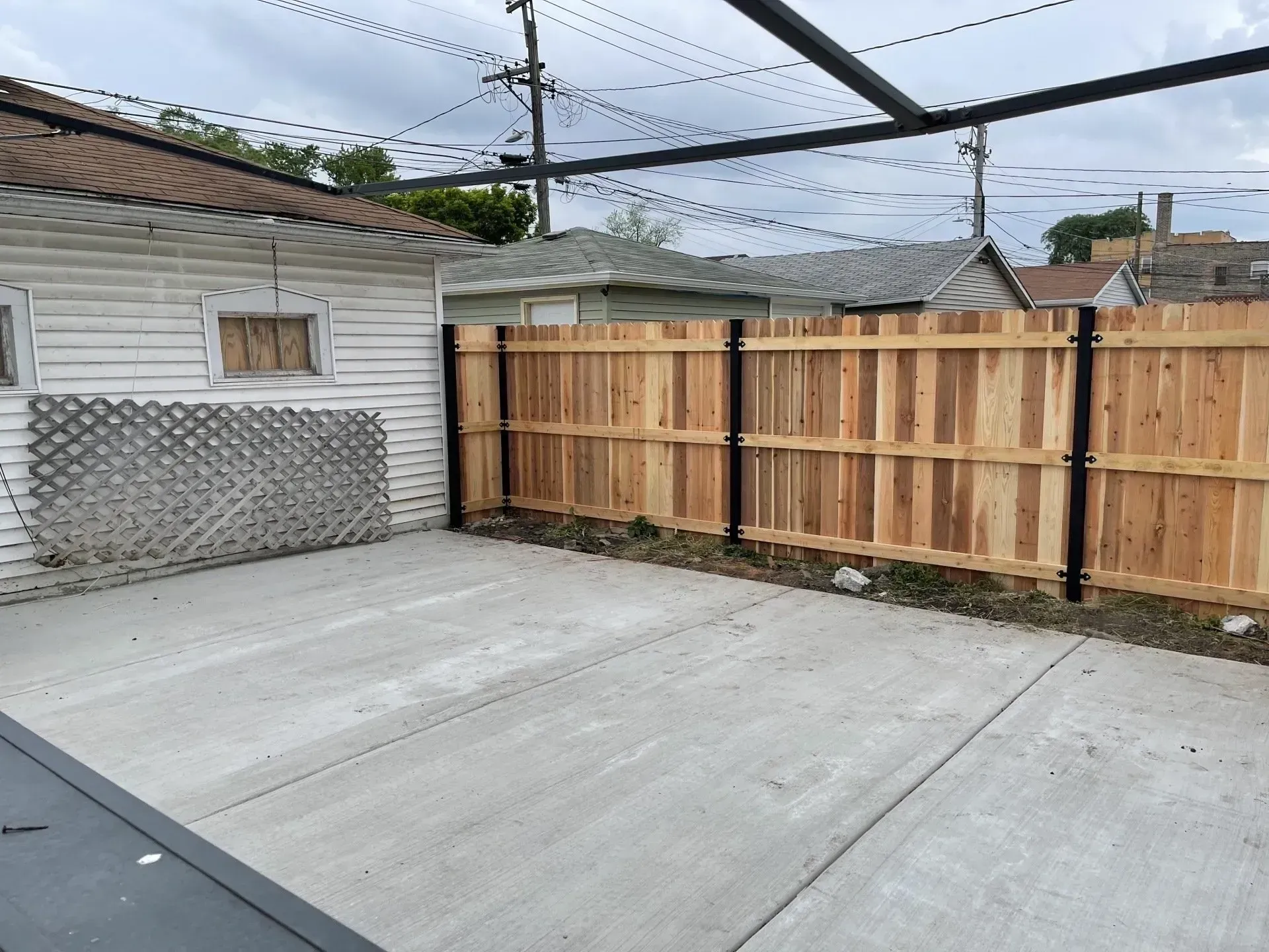 Fencing. Concrete patio next to a wooden fence and an old garage.