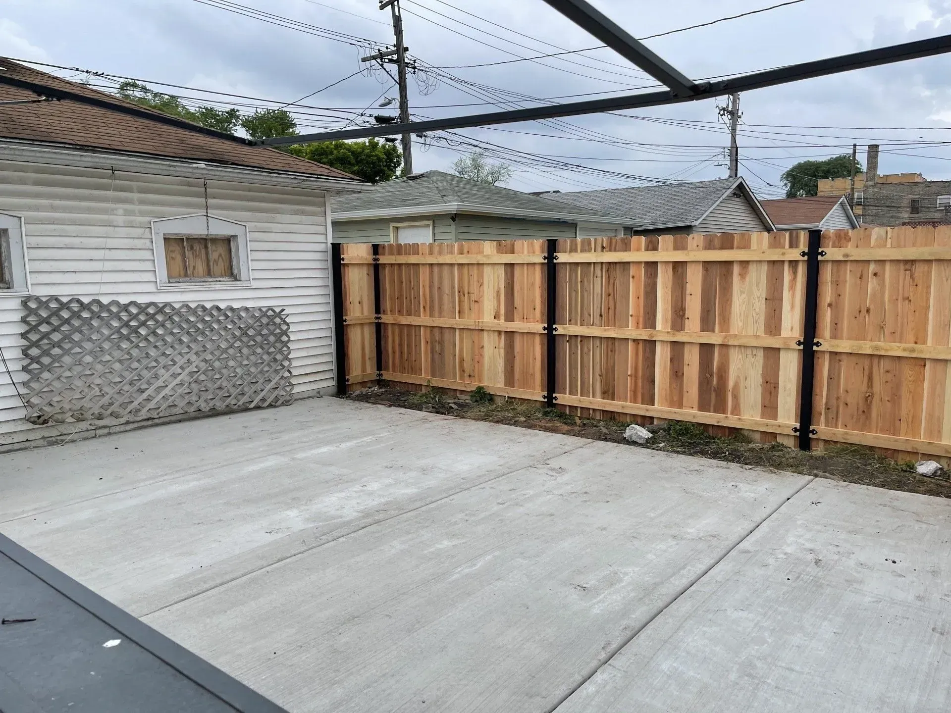 Gallery. Concrete backyard with a new wooden fence and a garage. Black metal posts.
