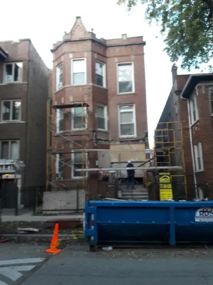 Gallery. Brown brick building undergoing renovations, with scaffolding, a blue dumpster, and orange cone in the foreground.