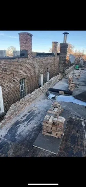 Gallery. Rooftop with brick chimneys, brick wall, and materials. Overcast sky.