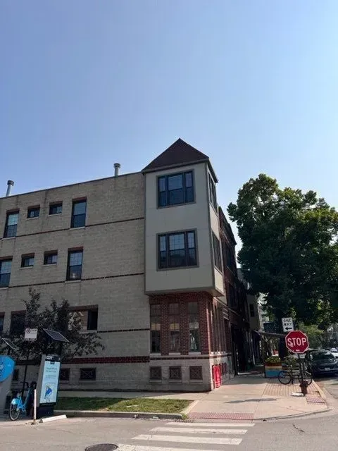 Multi-story brick building with corner tower and stop sign, on a sunny street.