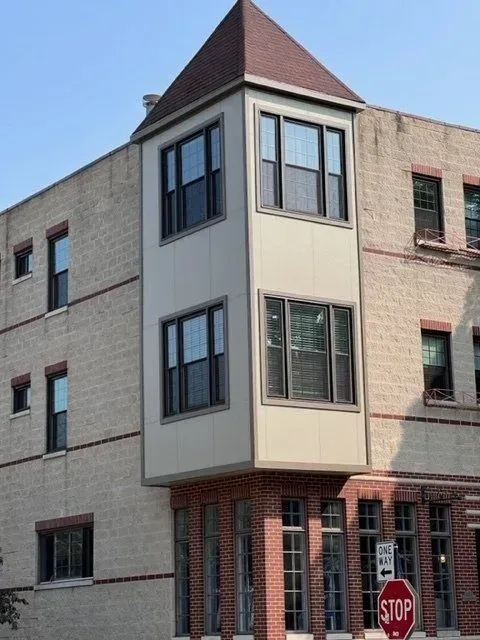Corner building with a projecting bay window, featuring brick and tan siding, and a stop sign.