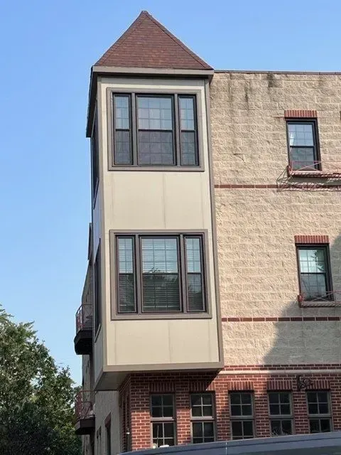 Exterior of a brick and tan building with a protruding bay window. Dark brown roof and window frames.