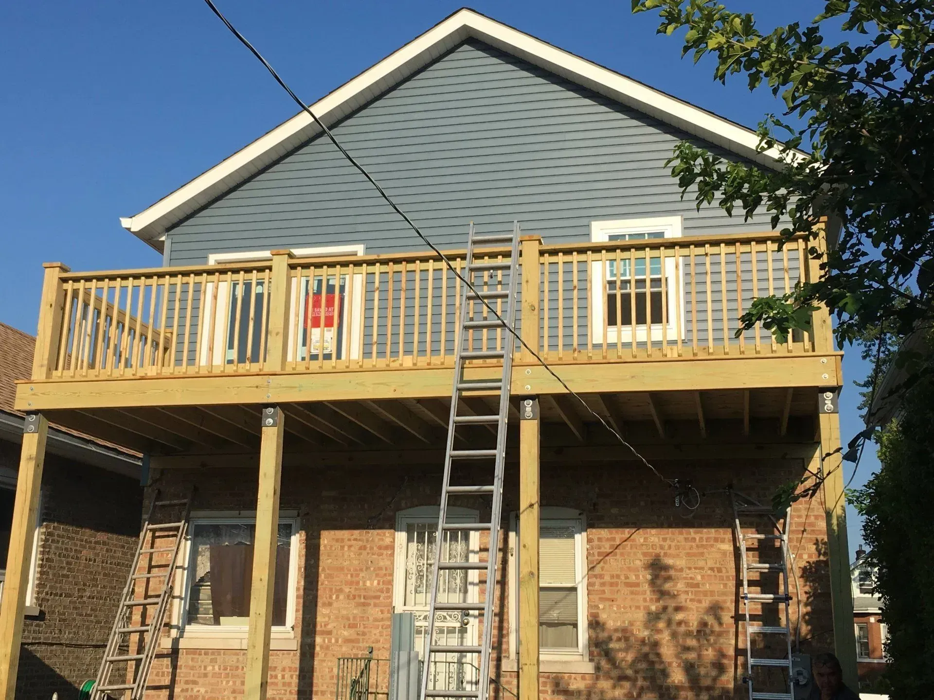 Gallery. Two-story house with blue siding, a wooden deck, and a ladder leading up to it.