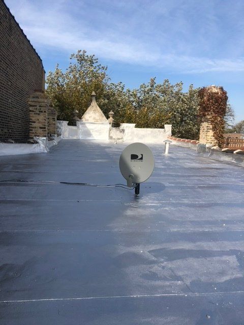 GARAGE. A rooftop with a satellite dish, against a blue sky with trees and a brick building.