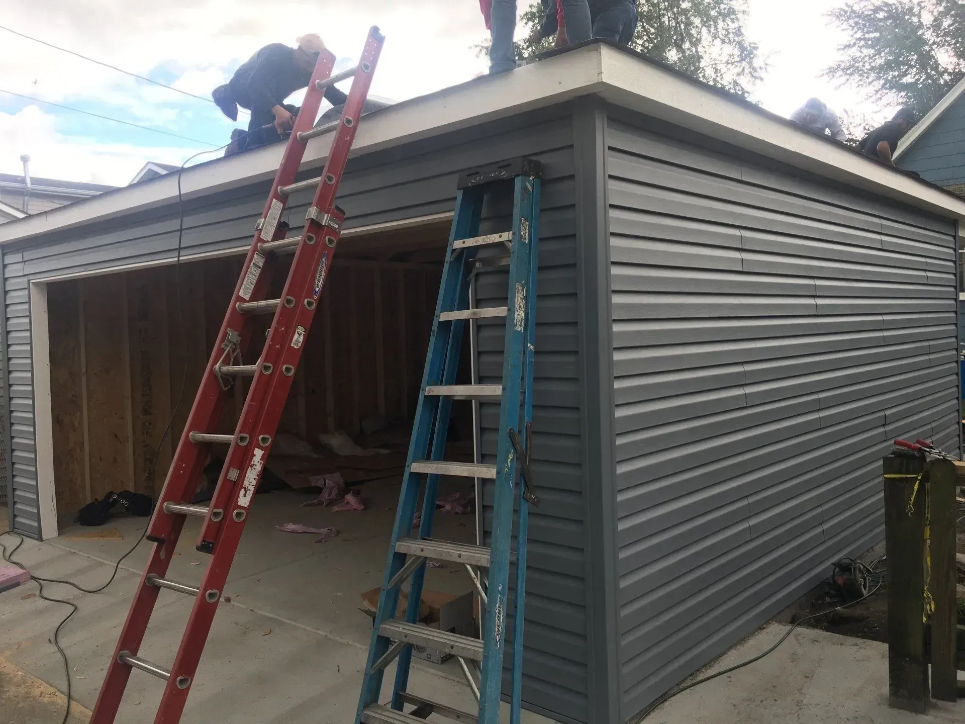 Gallery. Workers installing siding on a garage, using ladders. Grey siding and white trim.