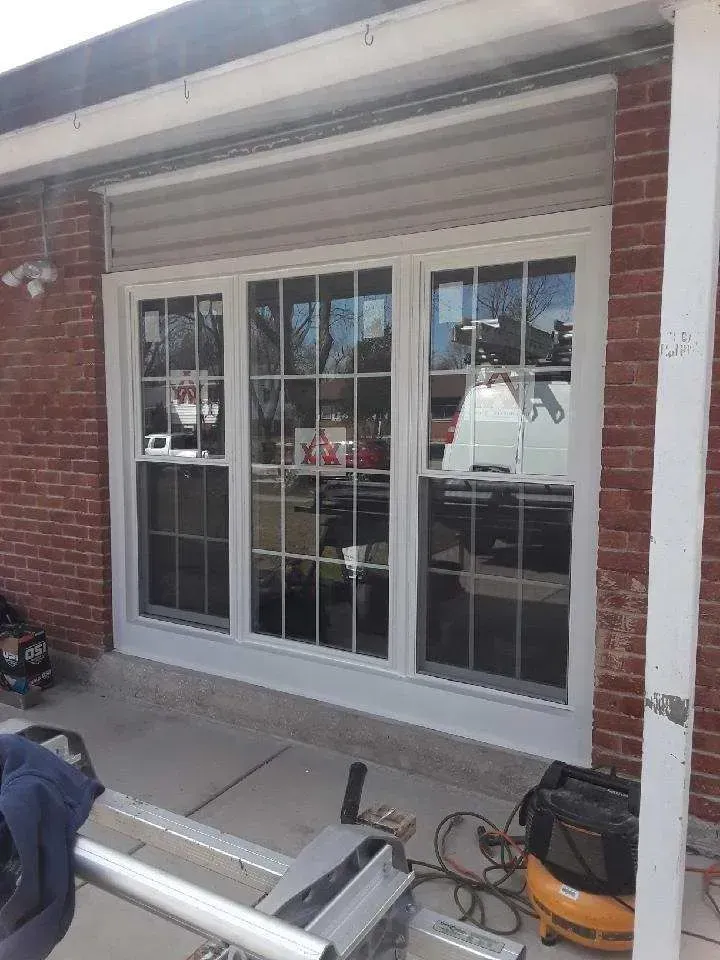 Gallery. Newly installed white-framed windows with grilles in a brick building under a covered area;
