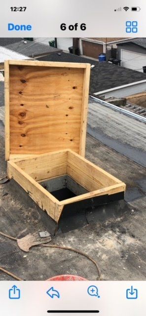 GARAGE. A wooden hatch on a flat roof, open. The hatch reveals a dark opening. Daylight visible.