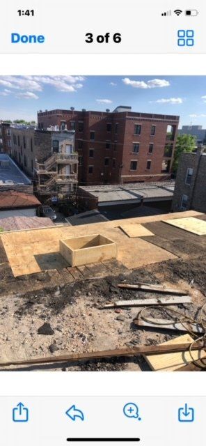 GARAGE. Construction site view from a rooftop. Wooden platform, dirt, buildings, and a sunny sky.