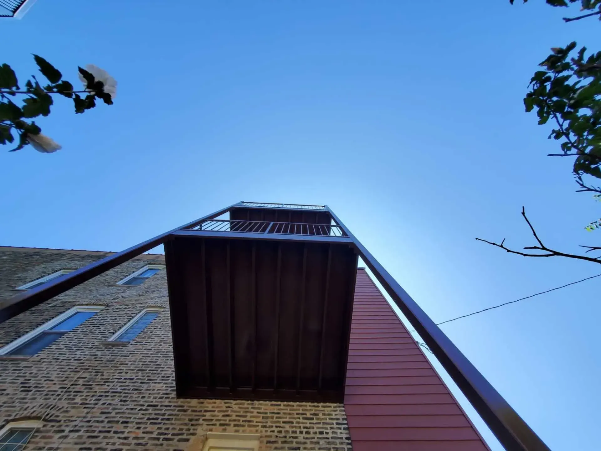 Gallery. Low-angle view of a brown wooden balcony extending from a brick building under a clear blue sky.