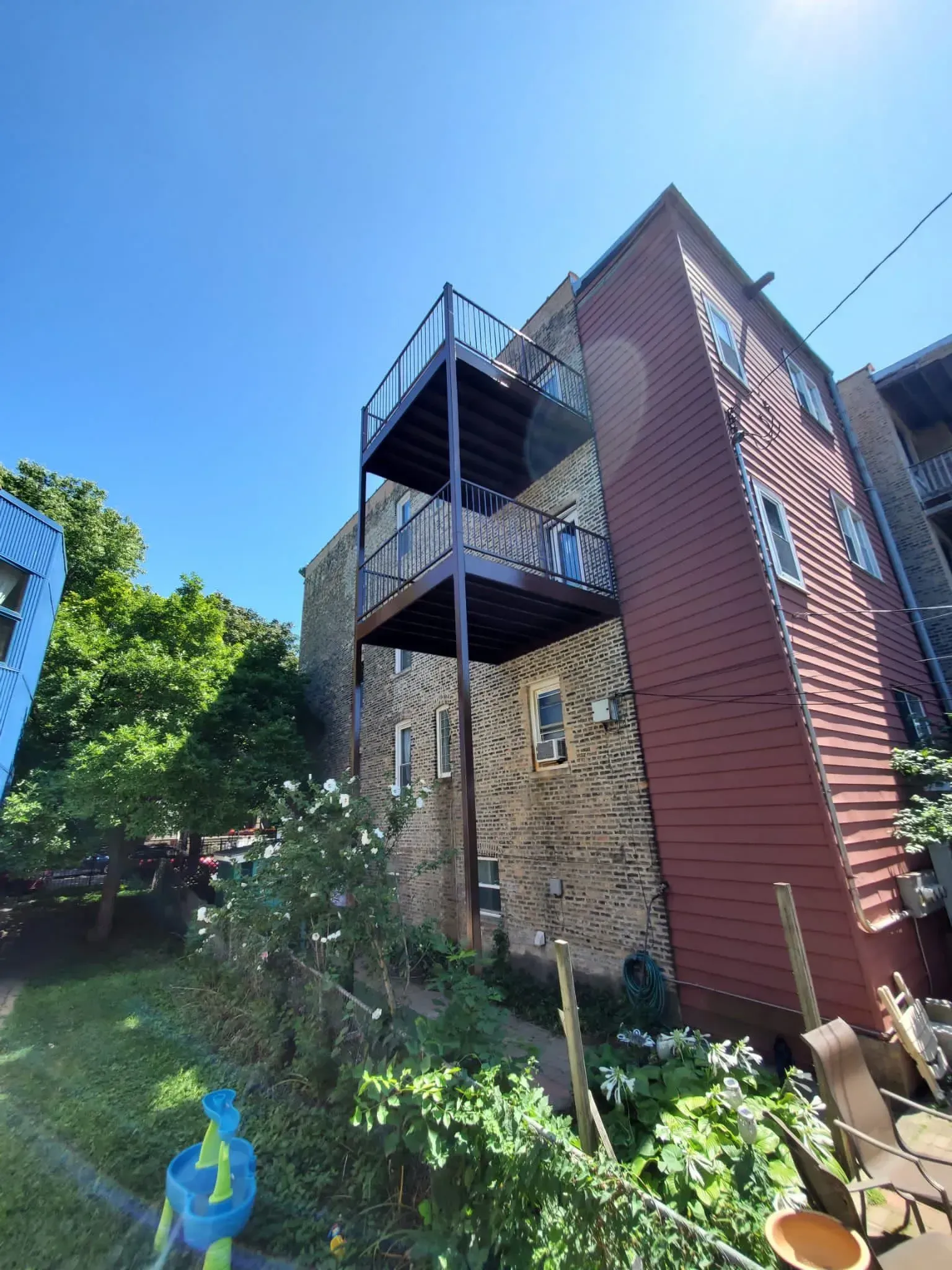 Gallery. Two-story metal balcony attached to a brick and wood building on a sunny day.