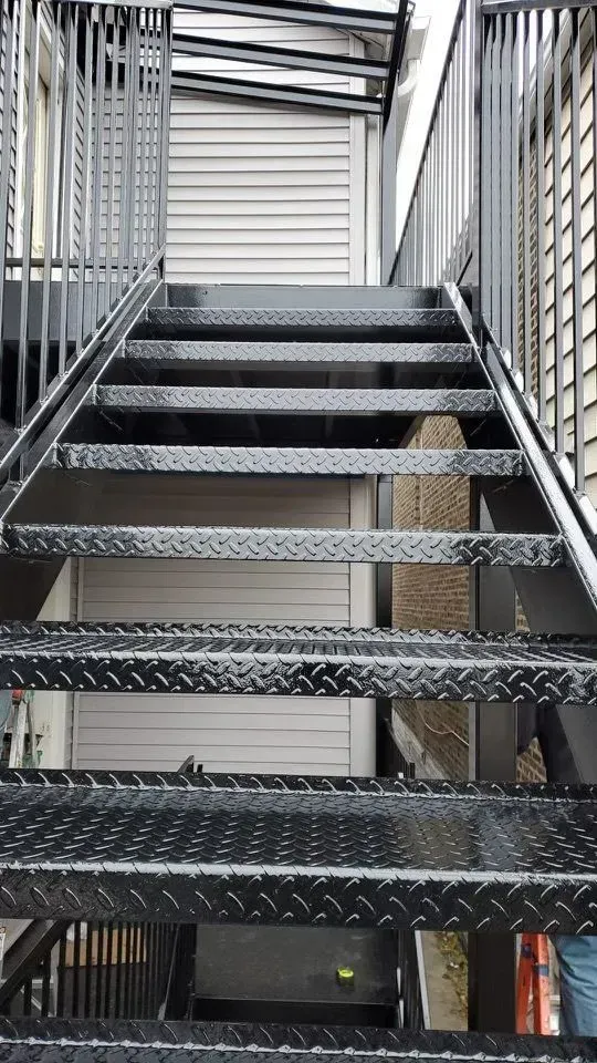 Gallery. Metal outdoor staircase with diamond-plate treads, leading upwards.