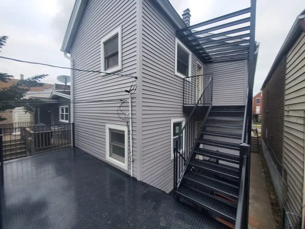 Gallery. Back of a two-story gray building with black metal fire escape stairs and a dark deck.