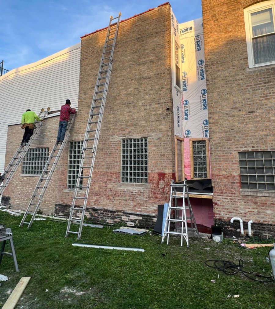 Construction workers on ladders renovating a brick building exterior.