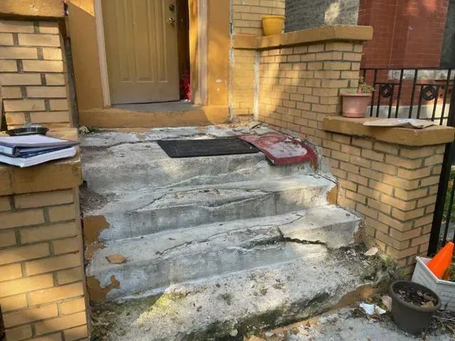 Gallery. Damaged concrete steps leading up to a house entrance. The steps are cracked and crumbling.
