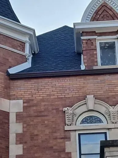Gallery. Brick building with dark blue shingle roof, white trim, and a decorative arched window.