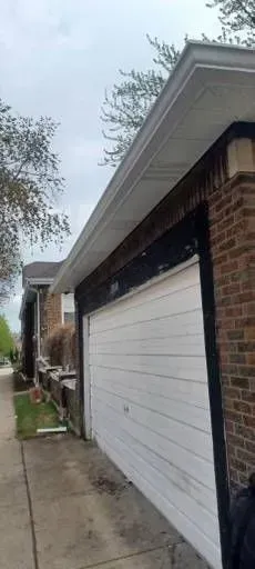 Gallery. Garage with white door, brick walls, and a sidewalk on a cloudy day.