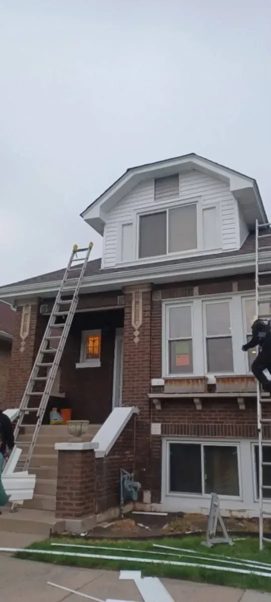 Gallery. Two-story brick house with white trim; ladders leaning against it. Cloudy sky, building renovation in progress.