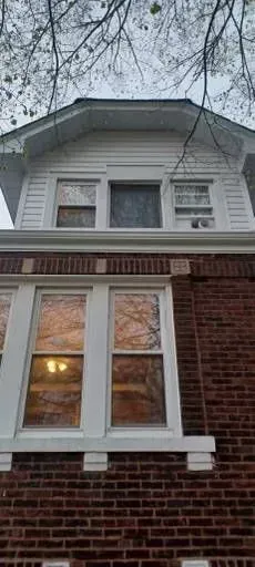 Gallery. A two-story brick building with white trim and windows, a cloudy sky, and tree branches overhead.
