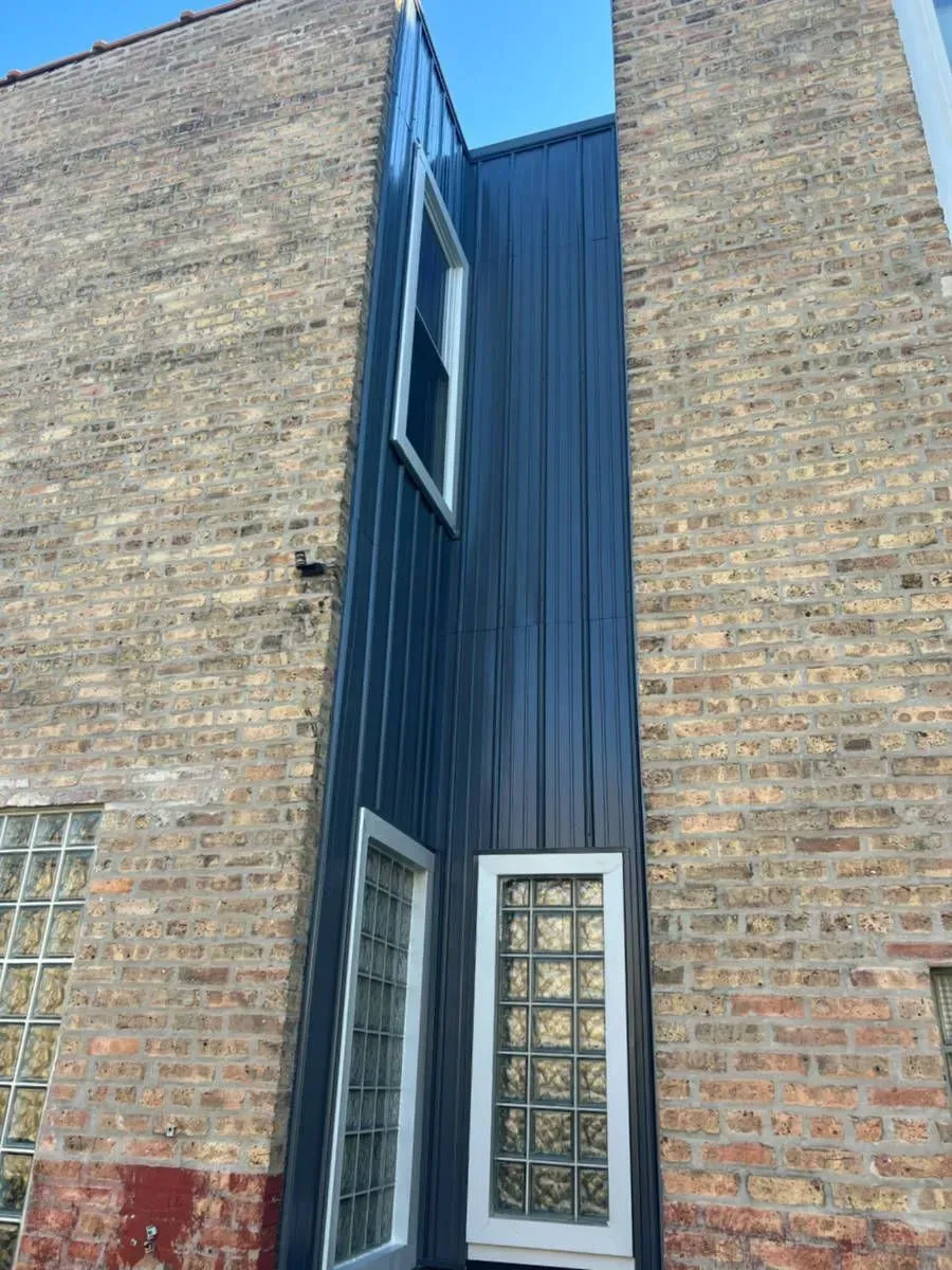 Narrow, dark blue metal siding between two brick buildings with two windows.