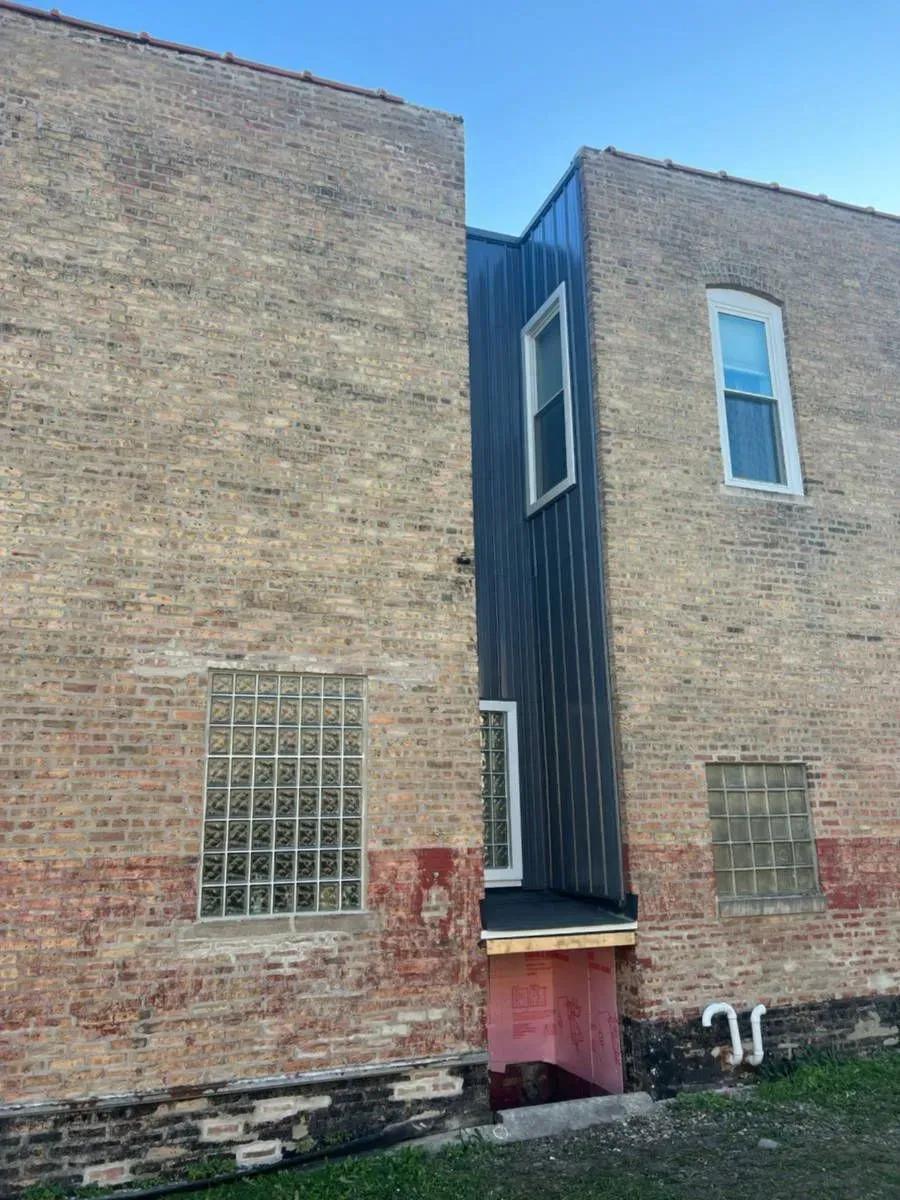 Brick buildings with a dark metal facade in between. Windows and a doorway are visible.