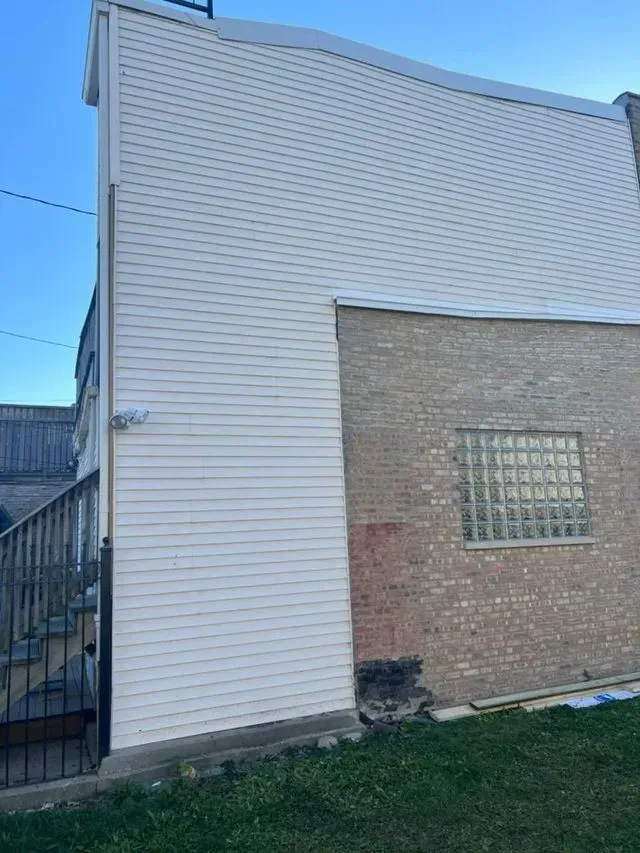 Back of a building with white siding and brick. Stairs and a small window are visible.