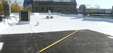 A rooftop with white sealant, an air conditioning unit, and a yellow pole lying across the darker surface.