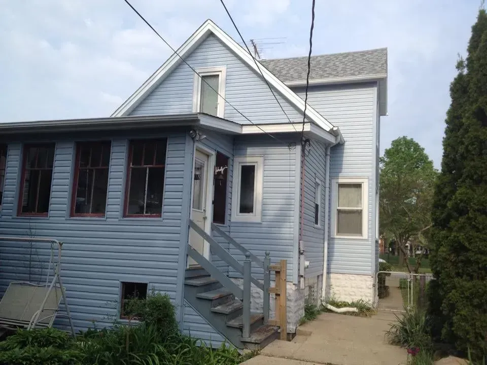 Blue house with porch and stairs, next to a concrete path and garden.