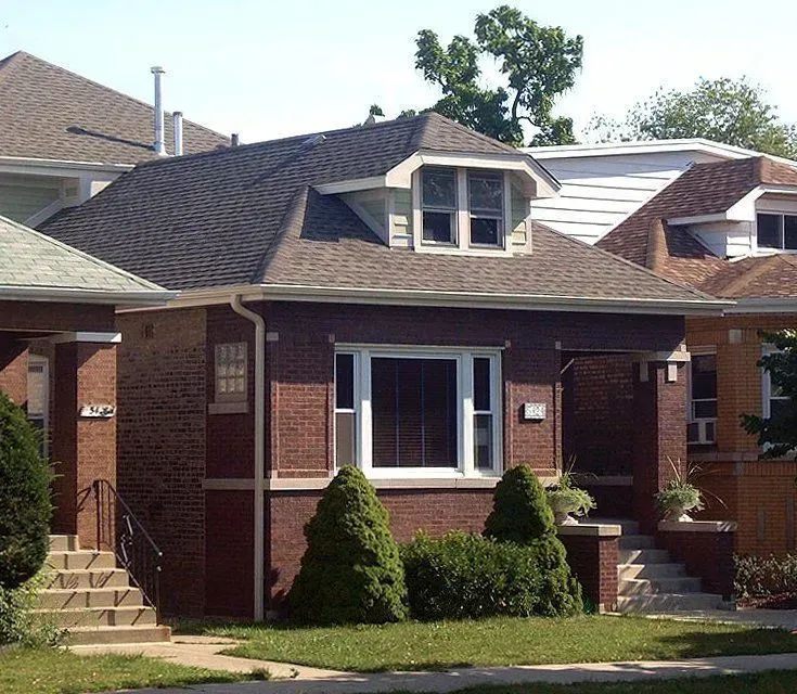 Red brick bungalow with a brown roof and a small front yard.