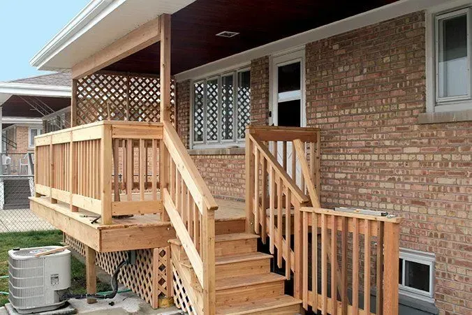 Wooden deck and stairs attached to a brick house. Lattice and railing accents are featured.