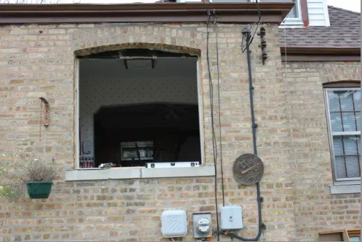 Exterior brick building with a large open window, electrical components, and a hanging planter.