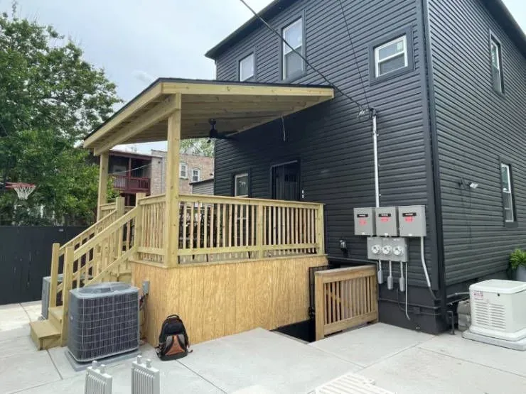 Gallery. Back of a two-story home with a wooden deck, ramp, and attached awning. Dark gray siding.