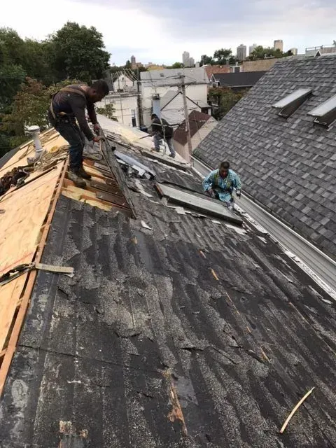 Gallery. Workers removing shingles from a weathered rooftop, securing safety lines.