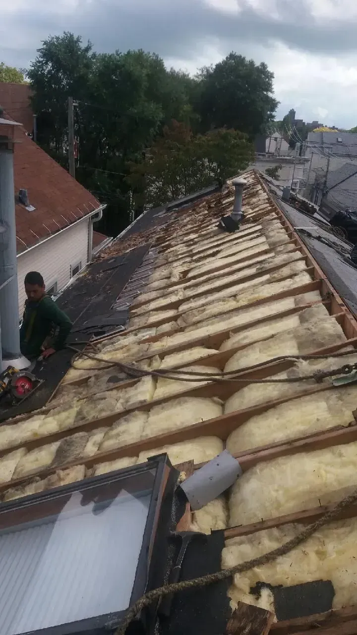 Gallery. Rooftop with exposed insulation and a person working; overcast sky, buildings in background.