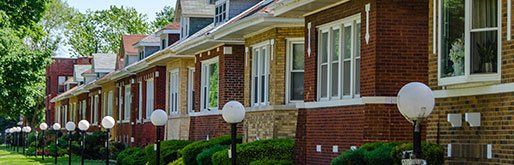 GALLERY. Row of brick houses with white windows and round streetlights in front.