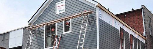 GALLERY. A building under construction with gray siding and ladders.