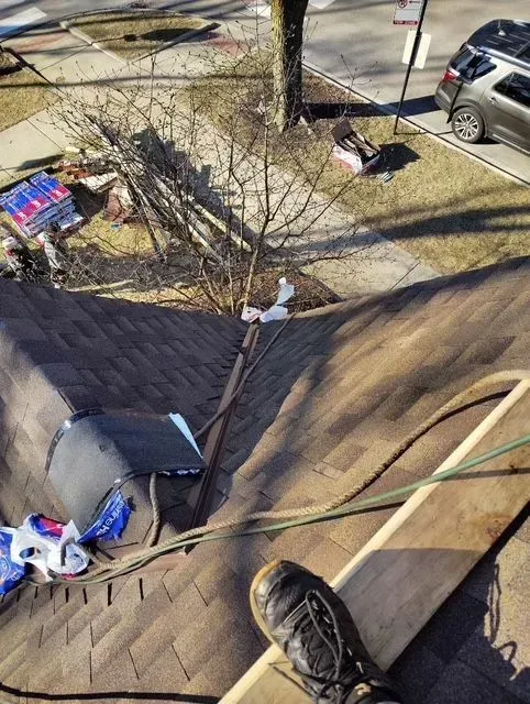 Gallery. View from a rooftop: person's foot on a board, debris on roof, street and car visible in background.