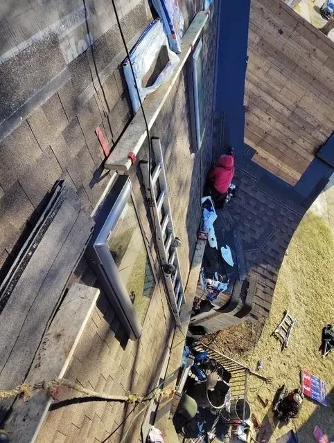 Gallery. View from above of a roof with a ladder and a person in red near a window, tools and debris scattered.