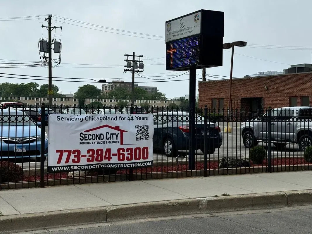 Gallery. A banner for Second City, a construction company, on a wrought iron fence in front of a building with a church sign.