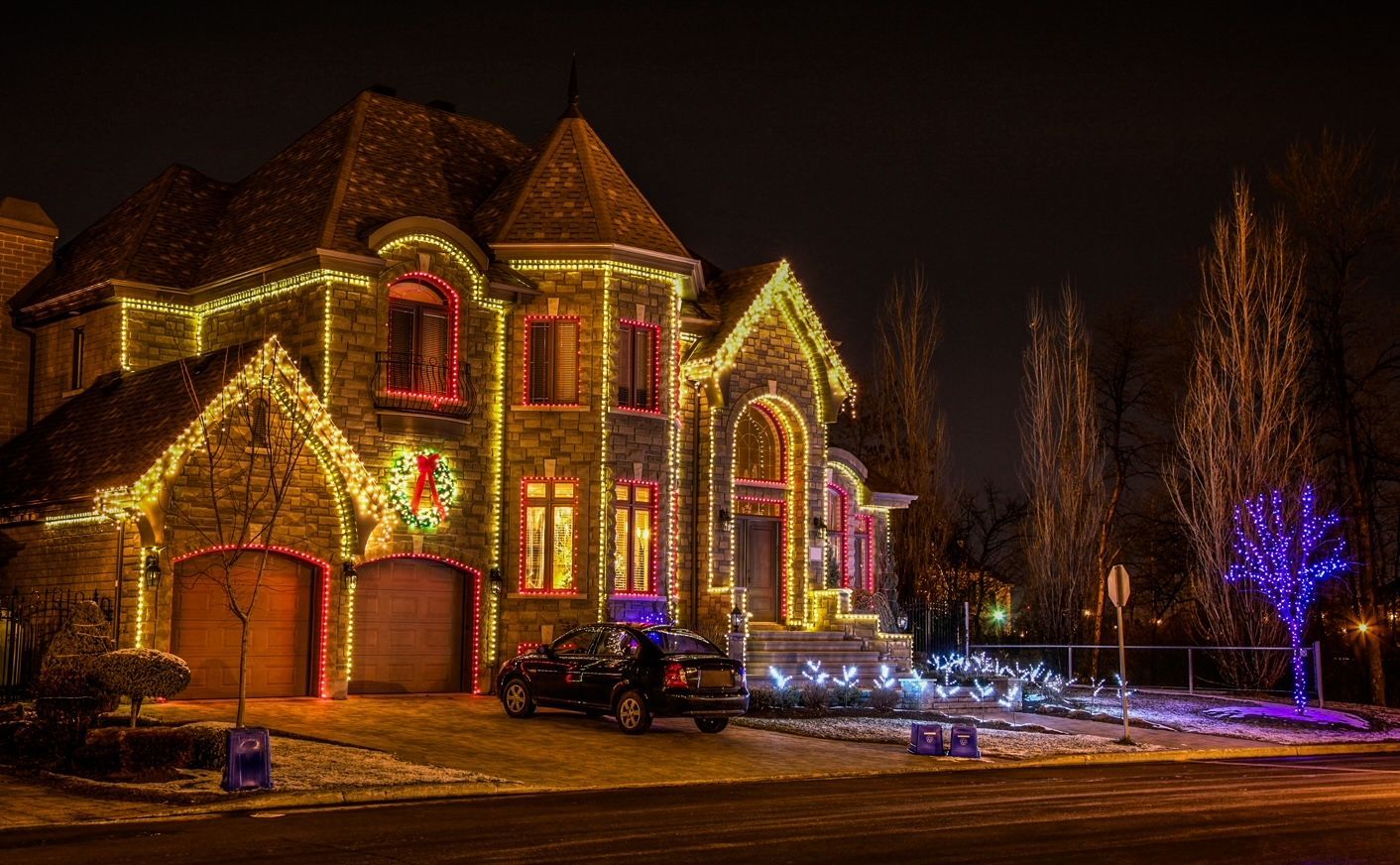 Stone home with Christmas lights on the roofline, windows and trees, by Seattle Holiday Lights