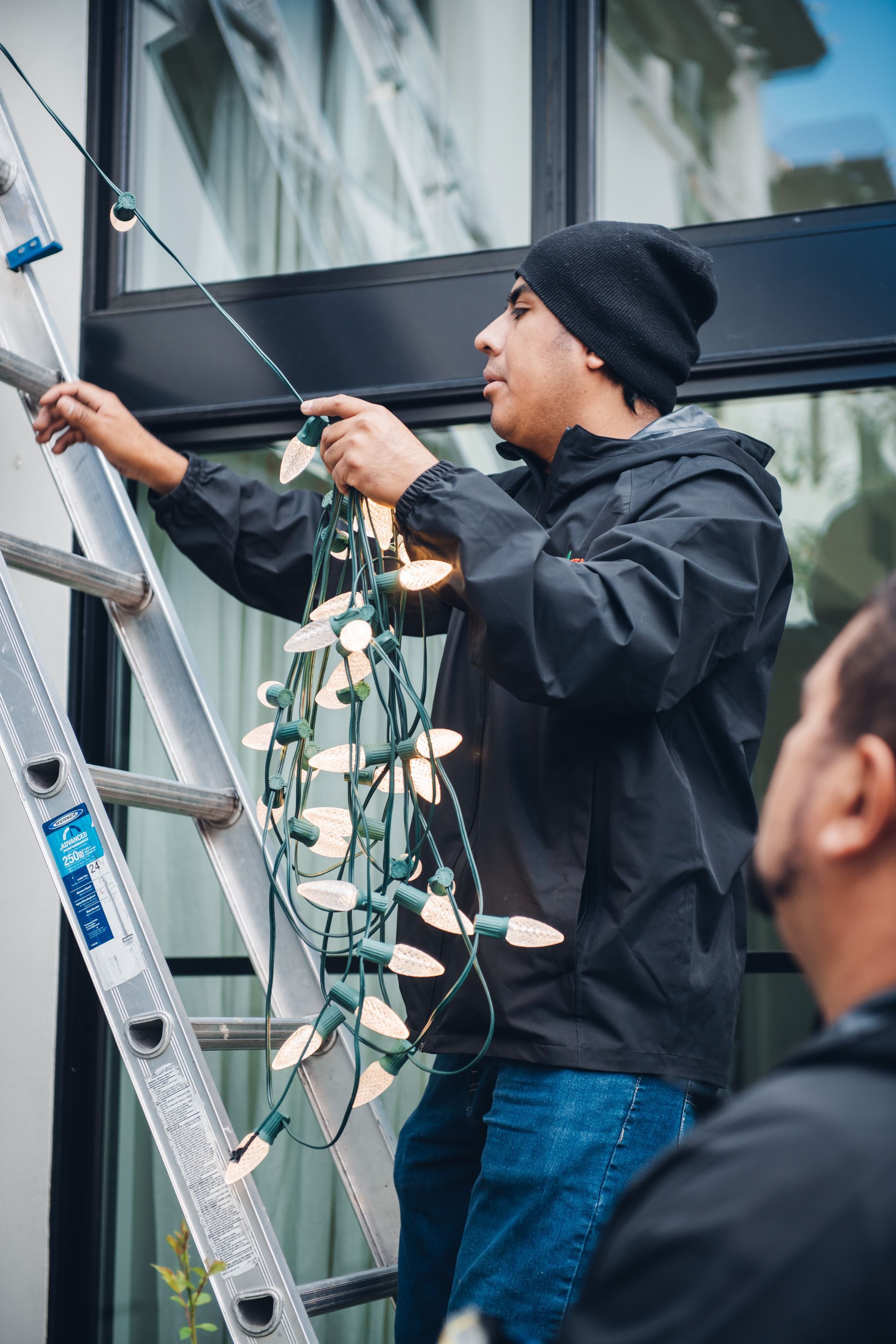 A man is standing on a ladder decorating christmas lights.