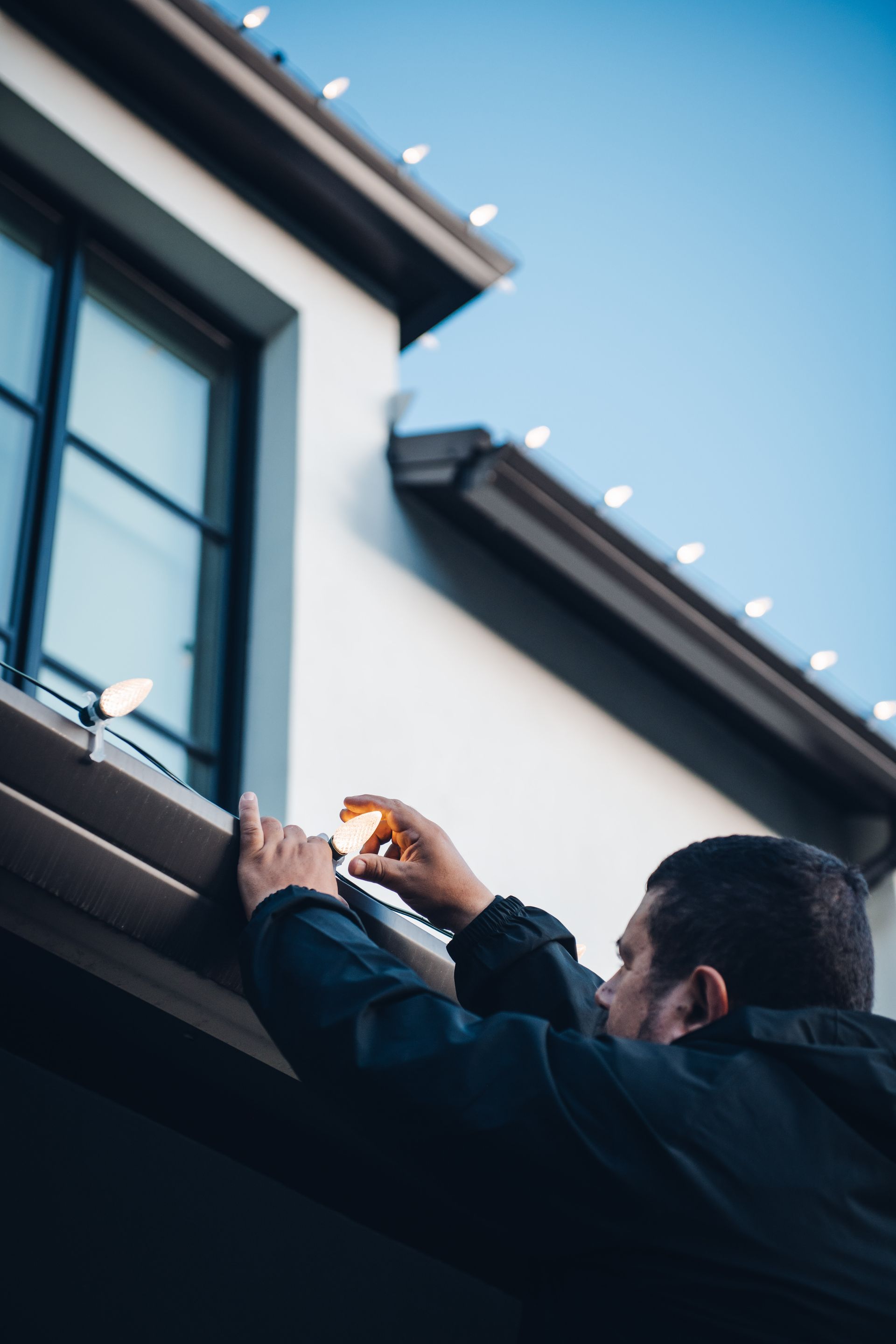A man is installing christmas lights on the side of a building.