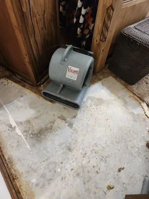 Gray air mover on a dirty concrete floor beside a wooden cabinet and wicker basket.