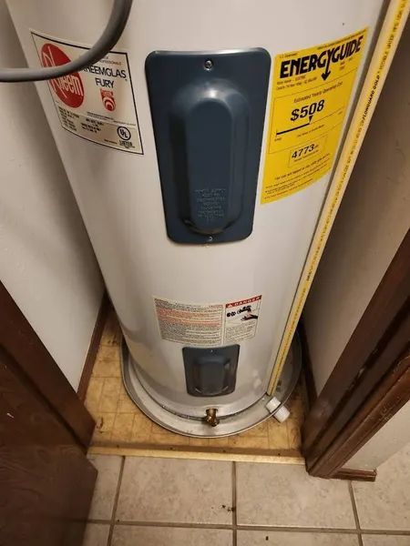 White water heater with blue control panel and yellow EnergyGuide label in a narrow closet.