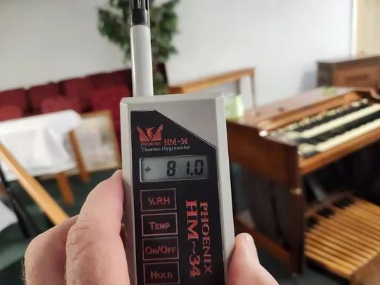 Hand holding a hygrometer reading 81.0 in a room with a keyboard in the background