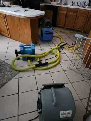 Kitchen with air mover fans and hoses on tiled floor, suggesting cleanup or water extraction.