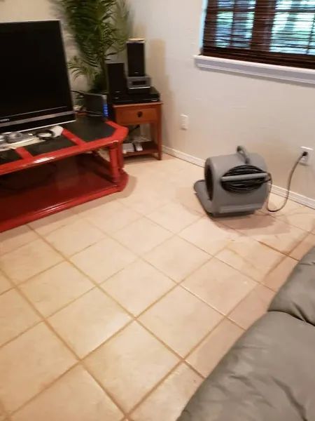 Living room with TV on red stand, tiled floor, couch edge, and a gray air mover near the window.
