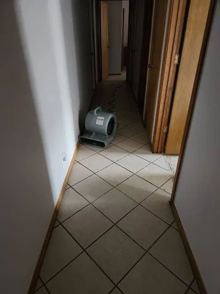 Narrow hallway with tiled floor and a gray air mover sitting on the floor