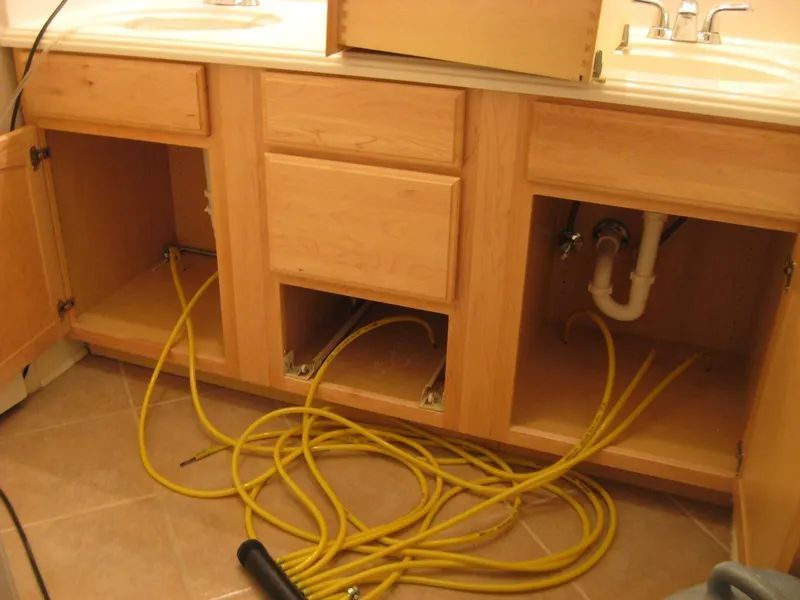 Kitchen sink cabinets with open doors and yellow cables tangled on the floor and in the cabinet openings